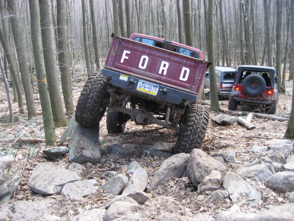 Maroon Ford pickup truck with large tires navigating rocks off-road