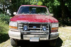1993 Ford Bronco - This red Ford Bronco is shown from the front, appearing to be covered in dust or mud.