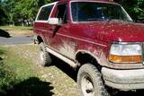 Red 1993 Ford Bronco covered in mud, front 3/4 view
