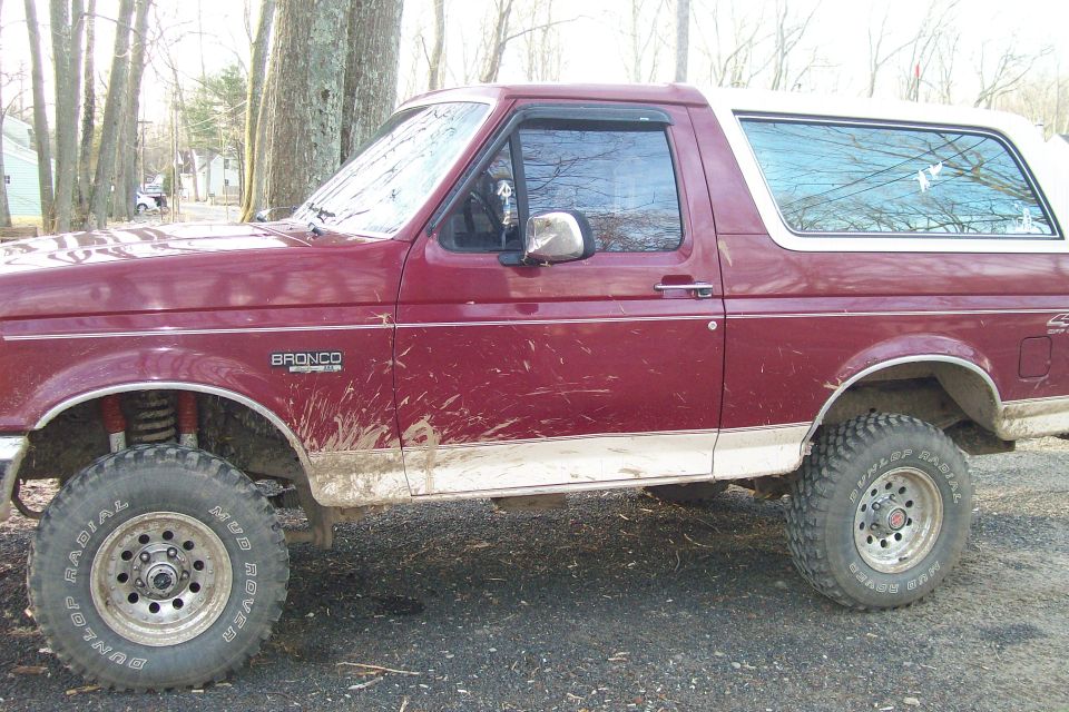 Maroon Ford Bronco with a white top, side view. Mud on the lower body