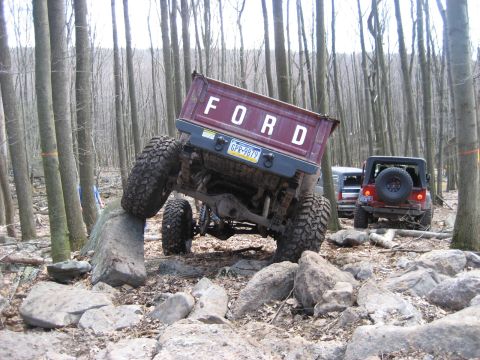 1991 Ford Bronco - A maroon Ford pickup truck navigates a rocky trail in a forest, with other vehicles visible in the background.