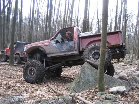 1991 Ford Bronco - Modified 1991 Ford Bronco tackling a challenging off-road course in a wooded area.