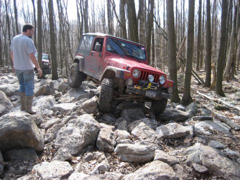 1991 Ford Bronco - A red Jeep Wrangler TJ Rubicon tackles a challenging rocky terrain in a wooded area.