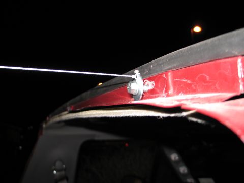 1995 Ford Bronco - Nighttime flash close-up of a thin braided steel cable anchored to the edge of a red fiberglass top or panel by a hex bolt with stacked was…