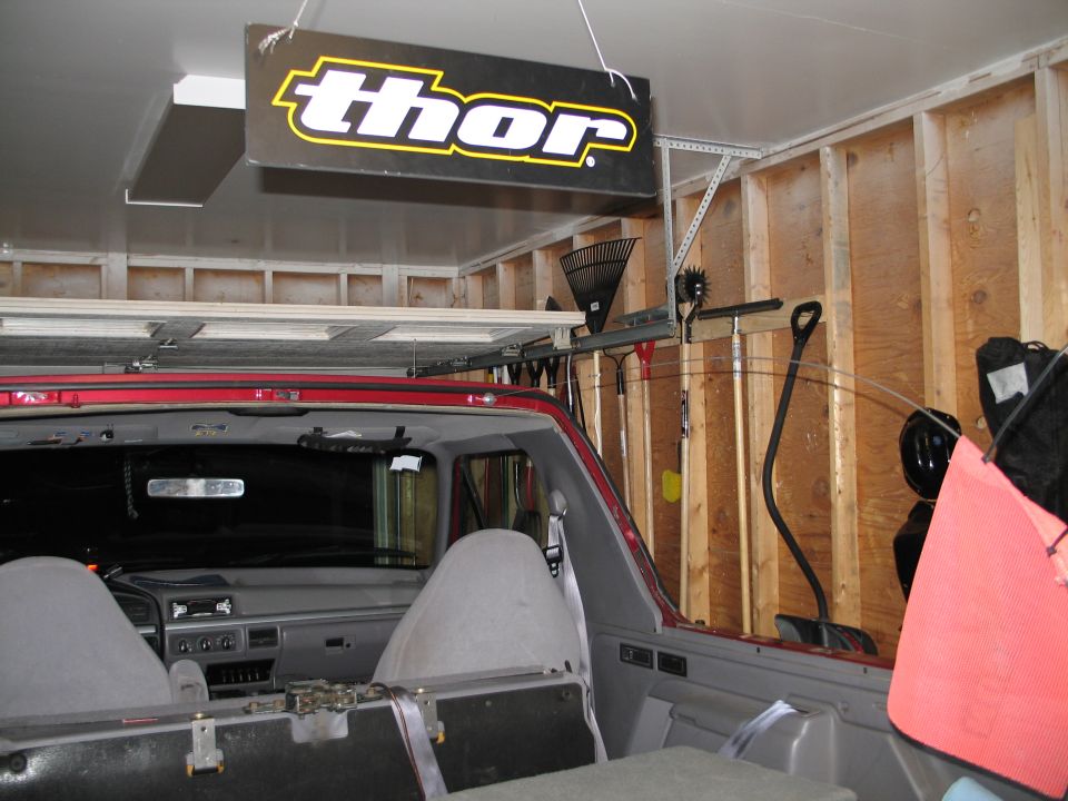 Interior of red Ford SUV with top removed, gray seats and dash, in a stud-wall garage under a Thor banner