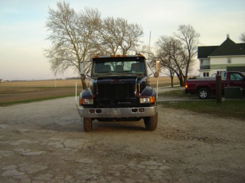 1992 Ford Bronco - A black truck is parked on a dirt lot in front of a house and fields.