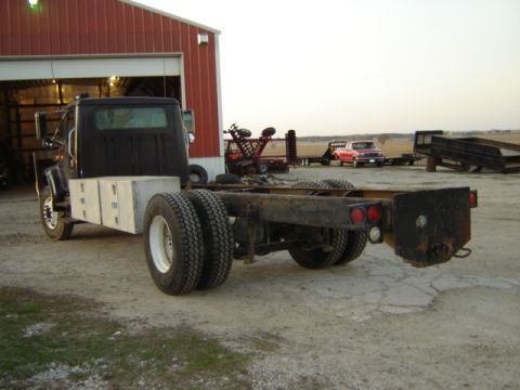 1992 Ford Bronco - A truck chassis sits outside a red barn with other vehicles and equipment in the background.