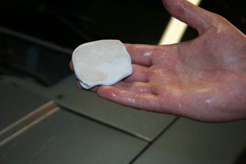 1990 Ford Mustang - A hand holds a piece of clay bar used for automotive detailing, with a car's surface visible below.
