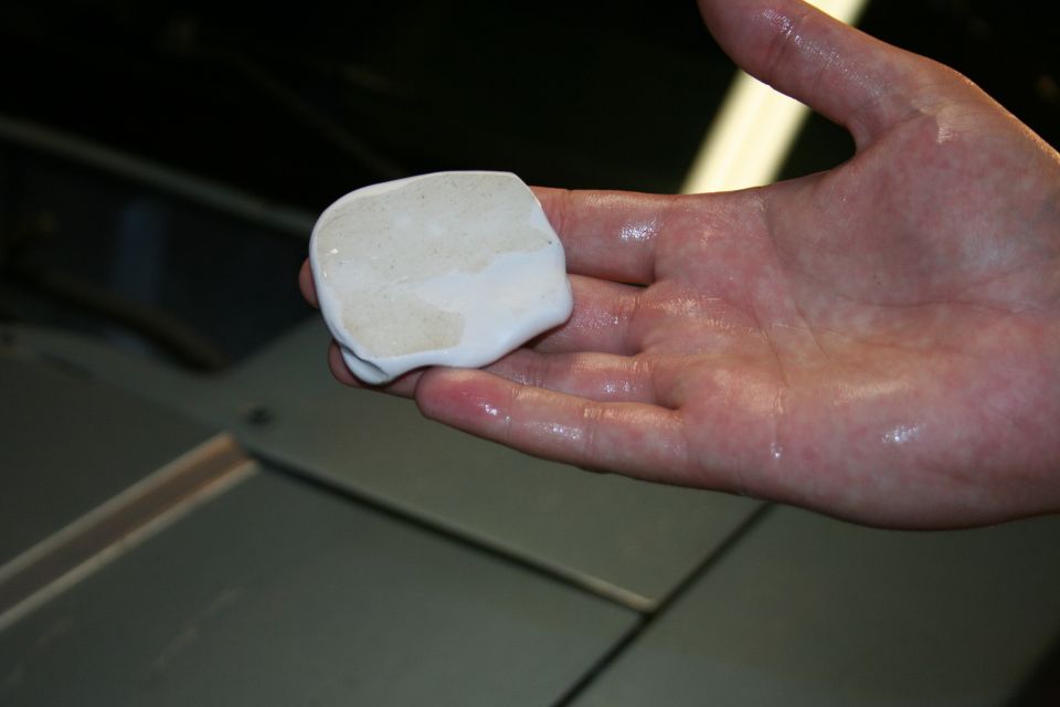 Hand holding a piece of white detailing clay over a car's hood