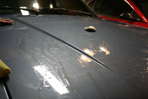 1990 Ford Mustang - A polishing stone rests on a wet car hood, with another vehicle visible behind it.