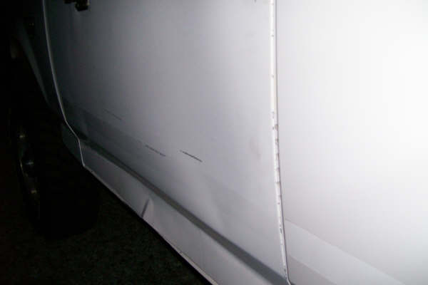 Close-up of scratches on the white lower door and rocker panel of a vehicle at night