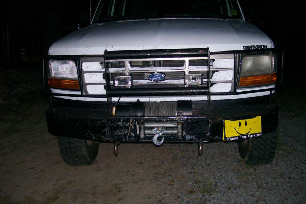 Front view of a white Ford truck with a brush guard, winch, and yellow smiley face license plate