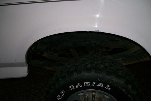 Rear wheel well and tire of a white truck. Text on tire reads 'OP RADIAL'