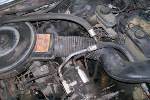 1992 Ford C-350 (Centurion Conversions) - Close-up view of an engine bay, showing various components and hoses. A warning label is visible on the air filter housing.