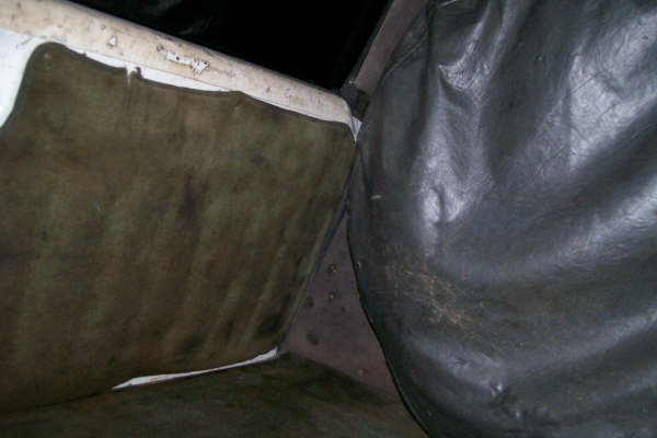 Close-up of worn carpeted interior panel and black vinyl-covered hump inside a vehicle