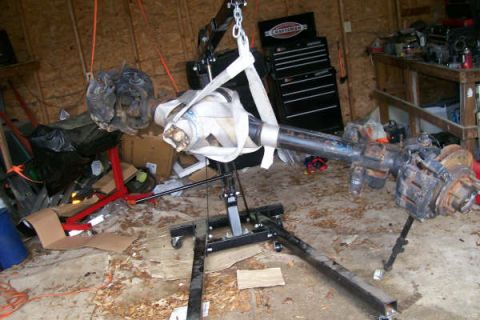 1988 Ford Bronco - A front axle assembly is suspended by an engine hoist in a cluttered garage setting.