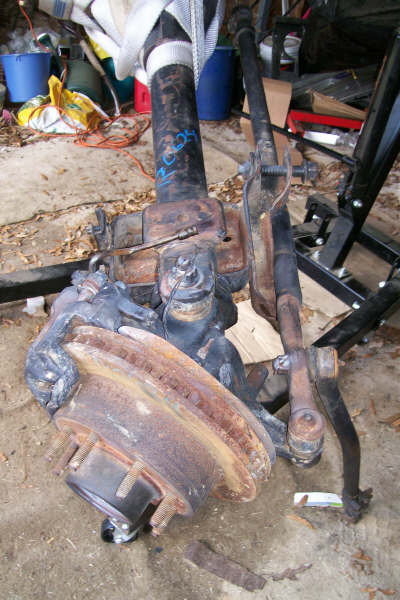 1988 Ford Bronco - Close-up of a Dana 60 front axle assembly, showing suspension parts and a rusty brake rotor.