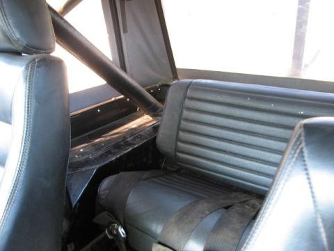 1986 Ford Bronco - Interior view of a vehicle showing black vinyl seats and a roll cage.