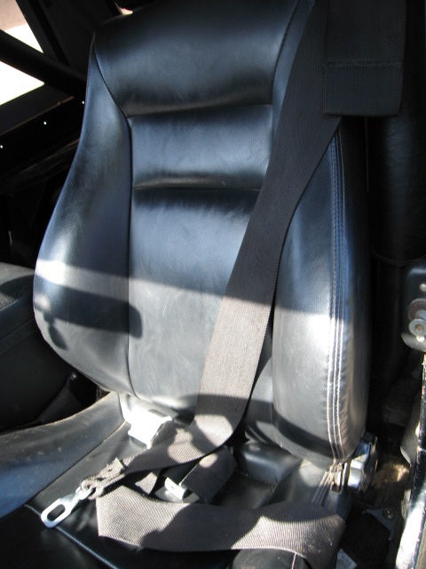 1986 Ford Bronco - Close-up of a vehicle's interior seat and seatbelt, with a website URL visible at the bottom.
