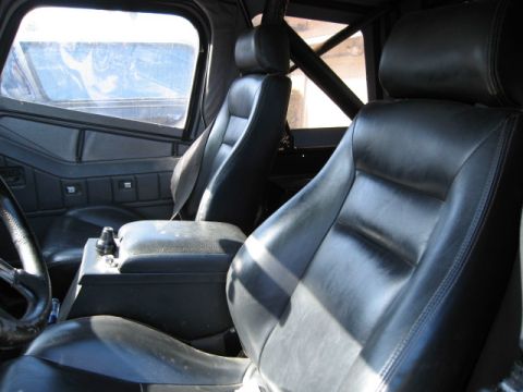 1986 Ford Bronco - The interior of a vehicle shows black leather seats and a center console with a gear shifter.