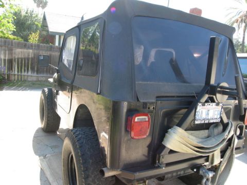 1986 Ford Bronco - Rear view of a black Jeep CJ with a soft top and a spare tire mounted on the back.