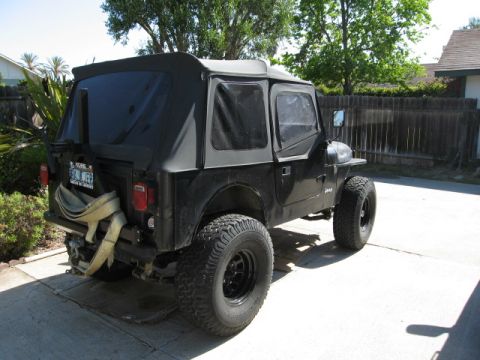 1986 Ford Bronco - This Jeep CJ is parked in a driveway with a wooden fence and trees in the background.