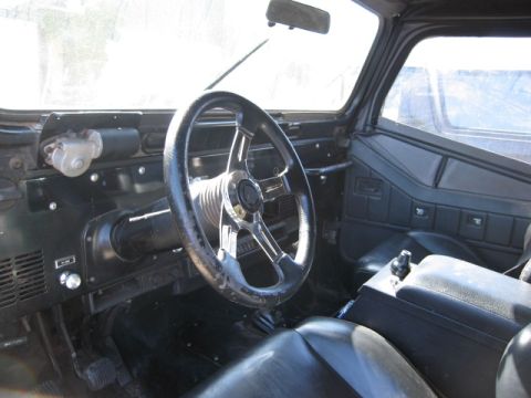 1986 Ford Bronco - The interior of a Jeep CJ shows a custom steering wheel and a central console with a shifter.