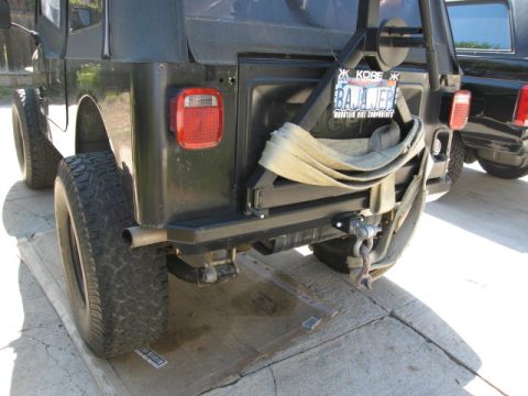 1986 Ford Bronco - Rear view of a black Jeep CJ7 showing its bumper, spare tire mount, and a strap. Another vehicle is visible to the right.