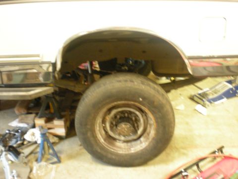 1993 Ford Bronco - The rear wheel and fender well of a white 1993 Ford Bronco are visible, supported by jack stands.