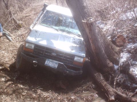 1990 Ford Ranger - A white 1990 Ford Ranger is stuck between two trees in a muddy, wooded area.