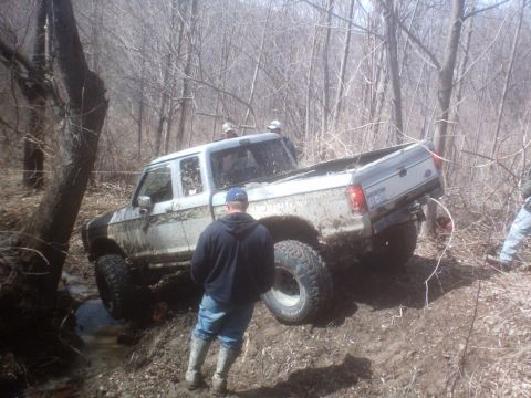 1990 Ford Ranger - A lifted Ford Ranger navigates a challenging muddy terrain in a wooded area.