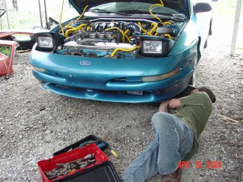 1993 Ford Probe - A mechanic works on the underside of a teal 1993 Ford Probe with its hood open.