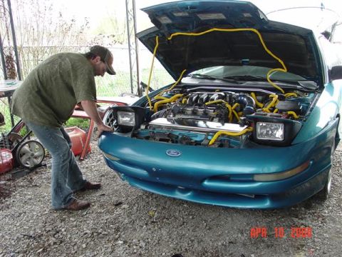 1993 Ford Probe - A man inspects the engine bay of a teal 1993 Ford Probe, which has its hood raised.