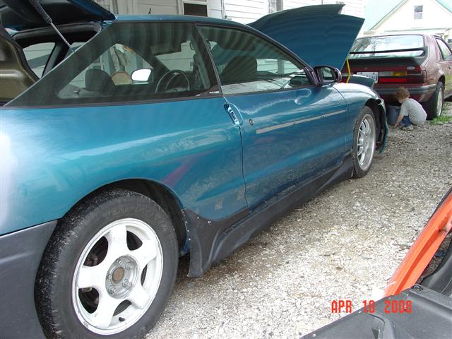 Teal 1993 Ford Probe coupe, driver's side view, hood and trunk open, parked on gravel