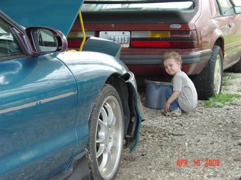 1993 Ford Probe - A child crouches near the rear of a red car, with the front quarter panel of a teal car visible in the foreground.