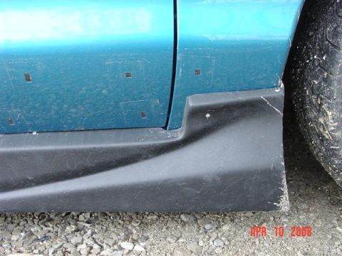 1993 Ford Probe - The side of a teal vehicle shows a black rocker panel and part of a tire, with evidence of tape on the body.