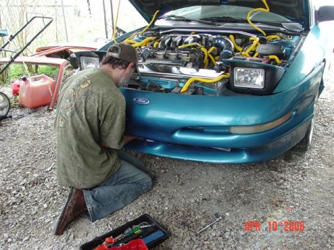 1993 Ford Probe - A person works on the engine of a teal 1993 Ford Probe with its hood open.