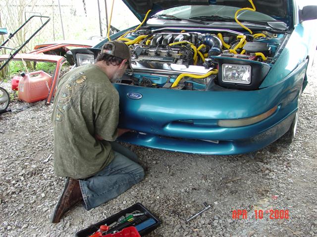 Teal 1993 Ford Probe with hood open, front view, showing engine and a person working on it