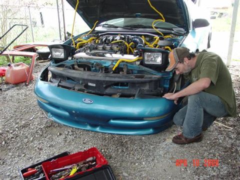 1993 Ford Probe - Man inspects the engine of a teal 1993 Ford Probe, with tools laid out nearby.