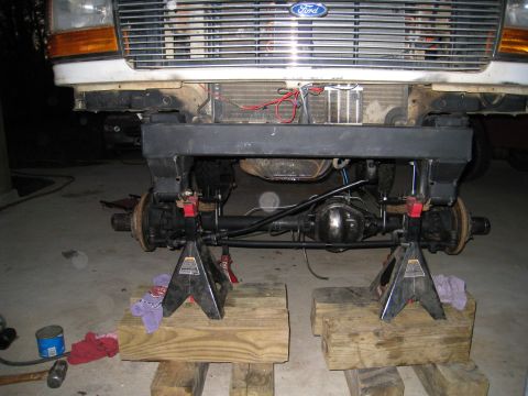 1996 Ford Bronco - Front axle of a Ford truck is supported by jack stands, revealing the suspension and differential components.