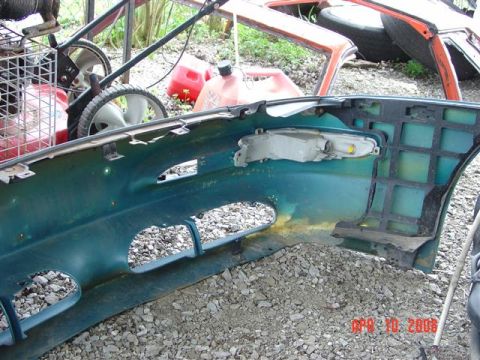 1993 Ford Probe - The interior of a car bumper shows its mounting points and a headlight assembly. Other vehicle parts and equipment are visible in the backg…