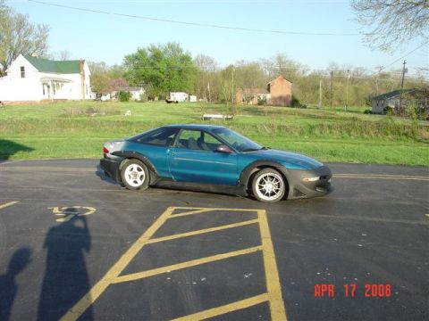 1993 Ford Probe - A teal coupe with body modifications is parked in a lot with houses in the background.