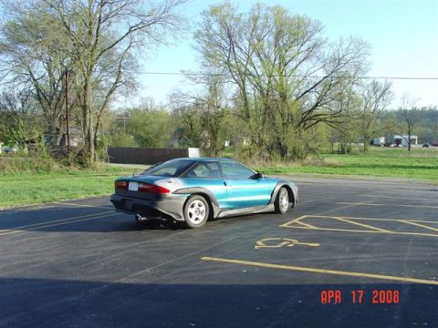 1993 Ford Probe - A teal 1993 Ford Probe is parked in a lot with trees and grass in the background.