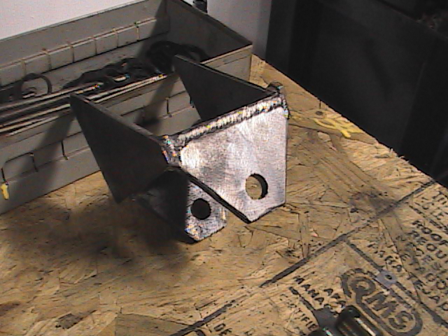 welded metal bracket on a wooden surface with a toolbox in the background