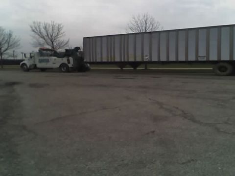 1992 Ford Bronco - A tow truck is preparing to haul a large trailer in a parking lot under an overcast sky.