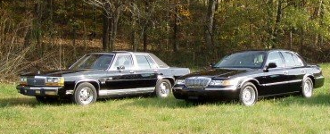 2001 Mercury Grand Marquis - Two black 2001 Mercury Grand Marquis sedans are shown parked on a grassy area with trees in the background.