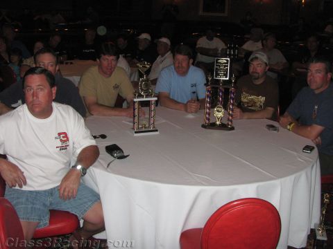 1990 Ford Bronco - Several people pose around a round white-clothed banquet table holding two awards trophies at an indoor event.