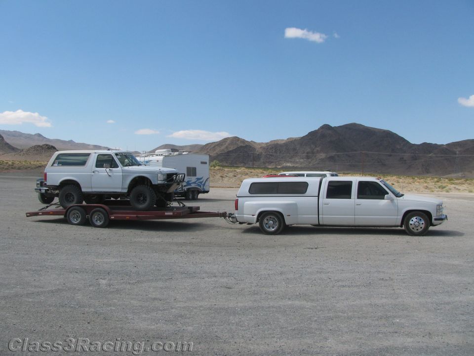 White dually pickup towing a trailer loaded with a Ford Bronco in the desert