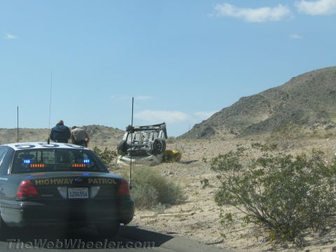 1990 Ford Bronco - California Highway Patrol Ford Crown Victoria cruiser is parked at the roadside near an overturned vehicle in the desert.