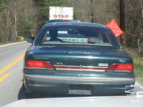 1985 Ford Crown Victoria LTD - The rear of a green Ford Crown Victoria is seen from behind, with a truck in the distance and a construction sign on the right.